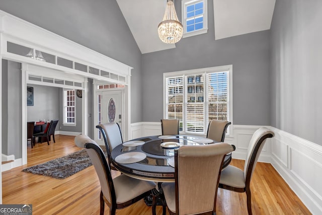 dining area featuring high vaulted ceiling, light wood-style flooring, an inviting chandelier, and a wainscoted wall