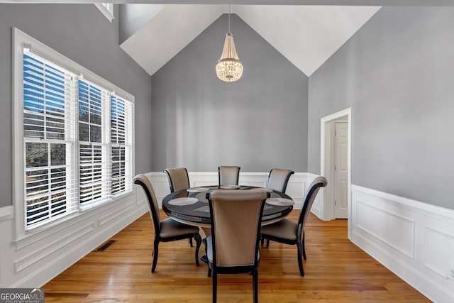 dining area with an inviting chandelier, a wainscoted wall, visible vents, high vaulted ceiling, and light wood finished floors