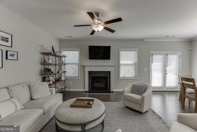 living area with ceiling fan, dark wood finished floors, visible vents, baseboards, and a glass covered fireplace