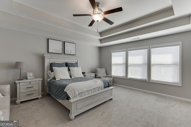 bedroom with a tray ceiling, visible vents, light carpet, and baseboards