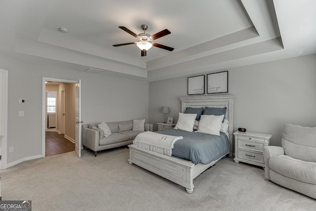 bedroom featuring light carpet, visible vents, baseboards, and a raised ceiling