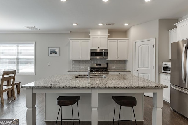 kitchen featuring stainless steel appliances, visible vents, a kitchen island with sink, white cabinetry, and light stone countertops