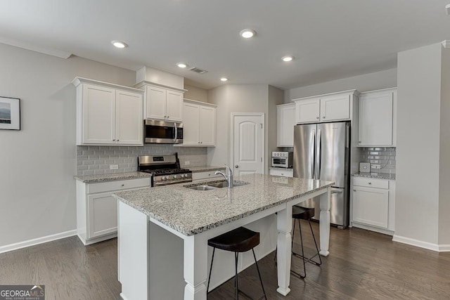 kitchen featuring a kitchen island with sink, a sink, white cabinets, appliances with stainless steel finishes, and light stone countertops