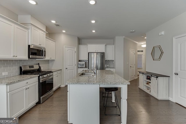 kitchen with stainless steel appliances, white cabinetry, and an island with sink