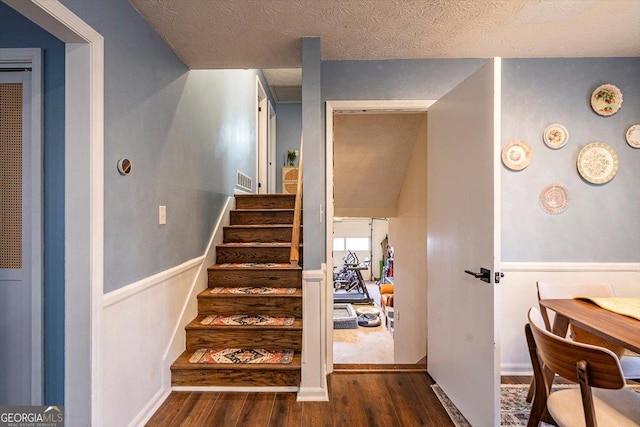 staircase featuring a wainscoted wall, a textured ceiling, and wood finished floors