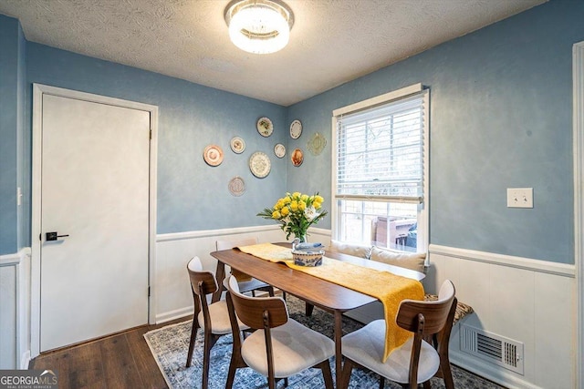 dining space with dark wood-type flooring, visible vents, a wainscoted wall, and a textured ceiling