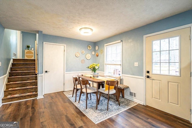 dining space with a wainscoted wall, dark wood-type flooring, stairway, and visible vents