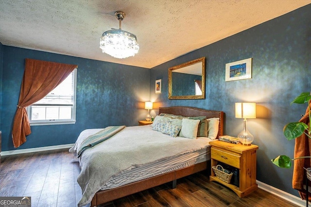 bedroom with a textured ceiling, an inviting chandelier, dark wood finished floors, and baseboards