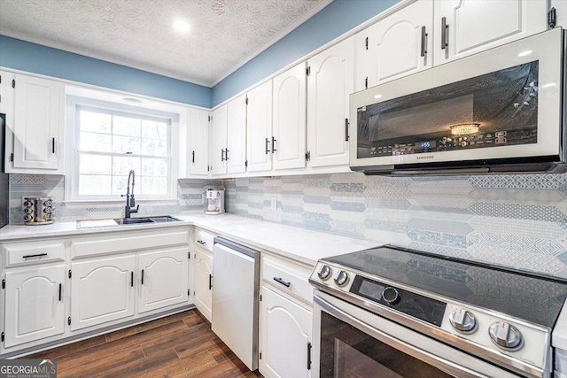 kitchen with appliances with stainless steel finishes, dark wood-style flooring, light countertops, white cabinetry, and a sink