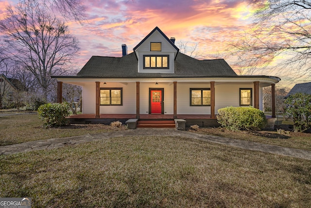 view of front of property featuring covered porch, a yard, and a chimney