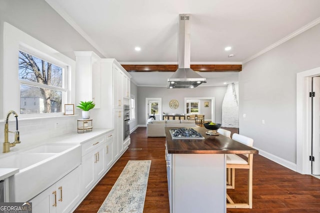 kitchen featuring white cabinets, butcher block counters, a breakfast bar area, open floor plan, and a sink