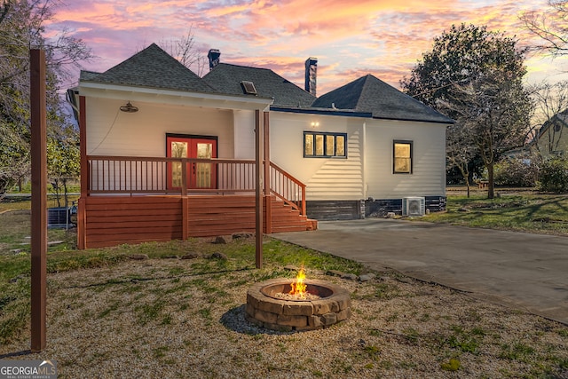 back of house at dusk with driveway, an outdoor fire pit, roof with shingles, and french doors