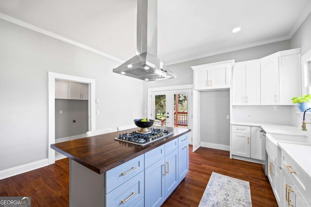 kitchen with island range hood, butcher block countertops, white cabinetry, appliances with stainless steel finishes, and a center island