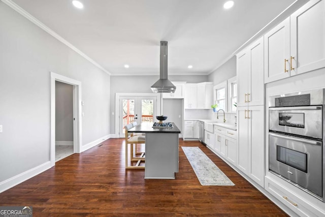 kitchen with a breakfast bar, island exhaust hood, stainless steel appliances, white cabinets, and a kitchen island