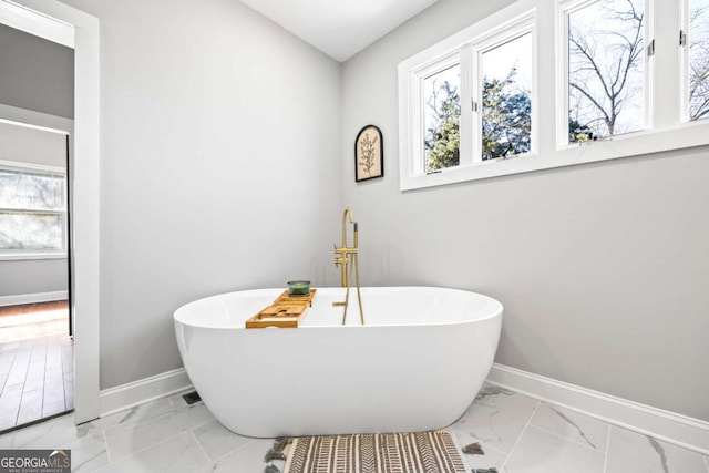 full bath featuring a soaking tub, a healthy amount of sunlight, marble finish floor, and baseboards