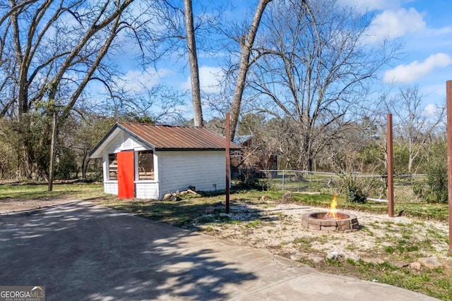 exterior space with fence, a fire pit, metal roof, and an outdoor structure