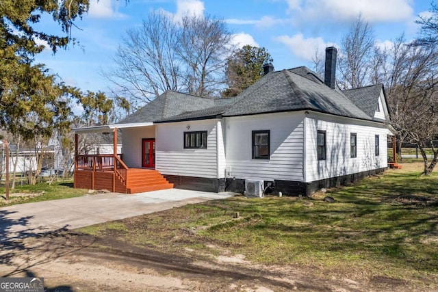 view of front of property featuring covered porch, a shingled roof, a front lawn, and central AC