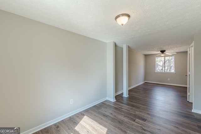 empty room with a ceiling fan, dark wood finished floors, a textured ceiling, and baseboards