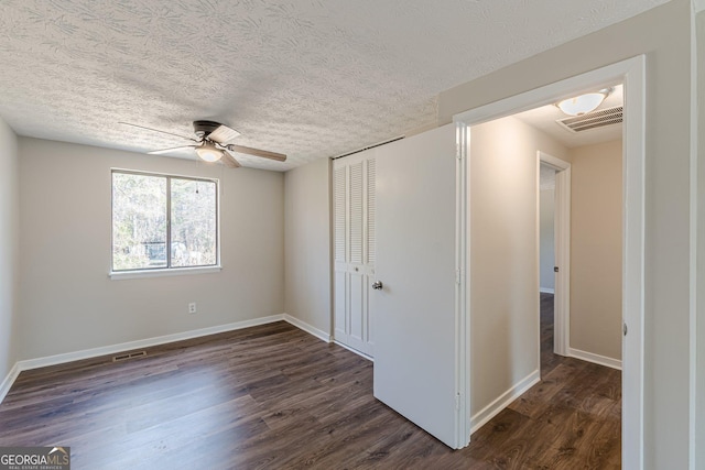 unfurnished bedroom featuring dark wood-style floors, a closet, visible vents, and baseboards