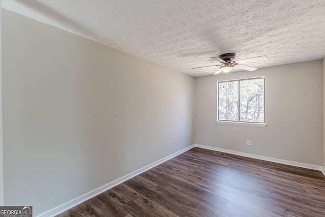 spare room with dark wood-style flooring, visible vents, ceiling fan, and baseboards