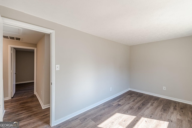 unfurnished room featuring dark wood-style flooring, visible vents, and baseboards