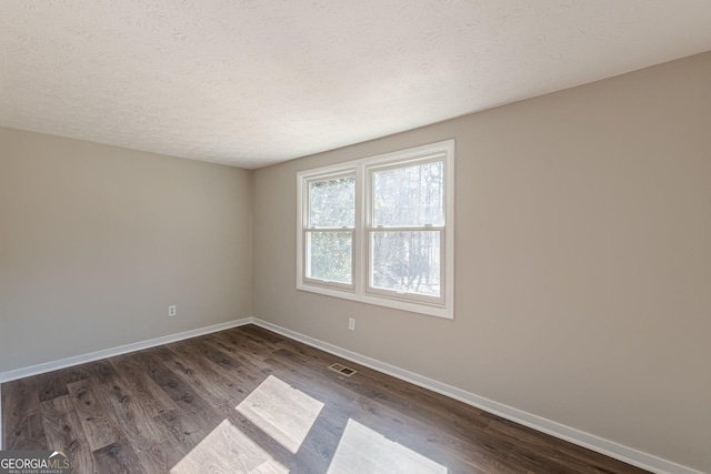 unfurnished room featuring dark wood-style floors, a textured ceiling, visible vents, and baseboards