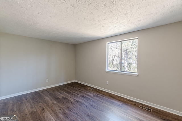 empty room featuring dark wood-type flooring, visible vents, a textured ceiling, and baseboards