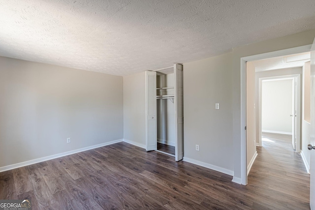 unfurnished bedroom with a closet, dark wood-style flooring, a textured ceiling, and baseboards