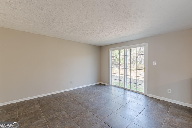 unfurnished room with a textured ceiling, baseboards, and dark tile patterned floors