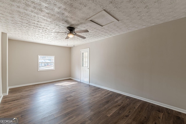 unfurnished room featuring a textured ceiling, dark wood-style flooring, attic access, and baseboards