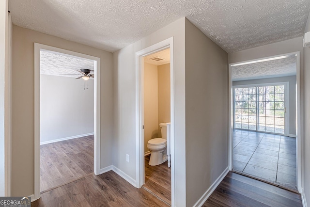 hallway featuring visible vents, a textured ceiling, baseboards, and wood finished floors