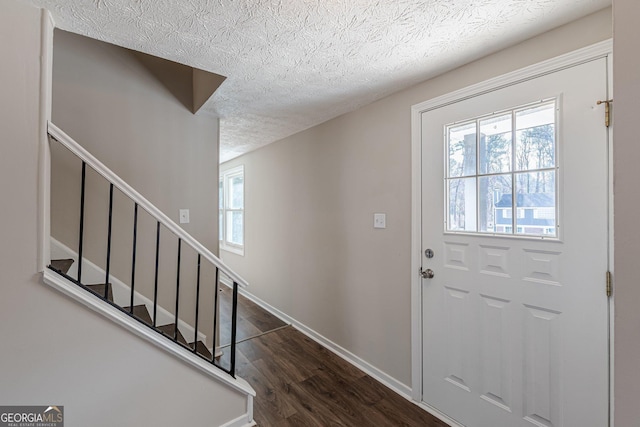 entrance foyer featuring a textured ceiling, stairway, dark wood-style flooring, and baseboards