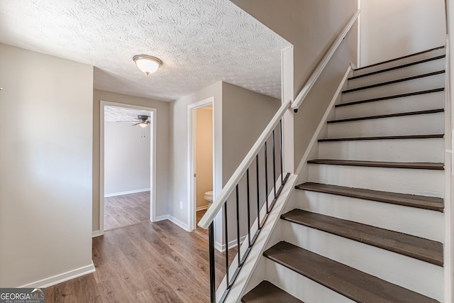 stairway featuring a textured ceiling, ceiling fan, wood finished floors, and baseboards