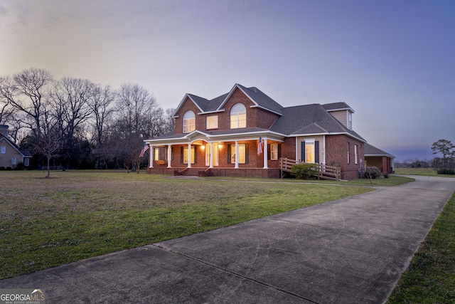 view of front of home with covered porch, a yard, and brick siding