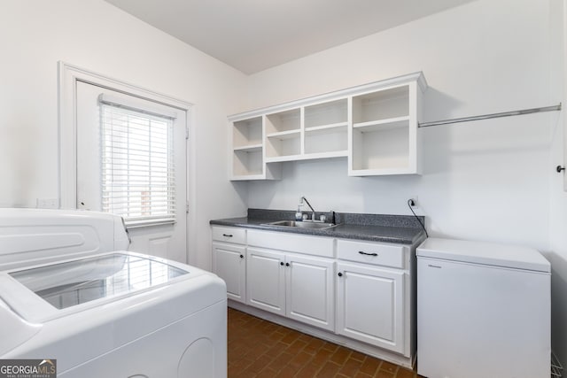 laundry area featuring brick floor, cabinet space, a sink, and washing machine and clothes dryer