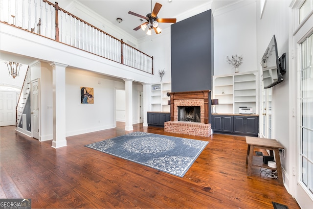 living room with crown molding, a brick fireplace, decorative columns, and dark wood-style floors