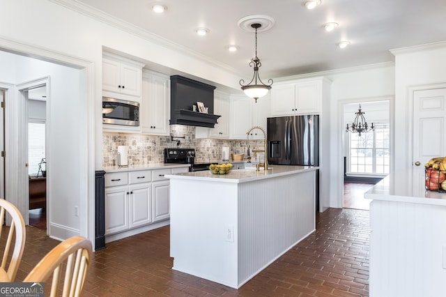 kitchen with stainless steel appliances, white cabinets, ornamental molding, an island with sink, and pendant lighting