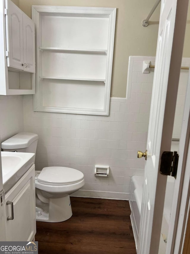 bathroom with toilet, wood finished floors, tile walls, and vanity