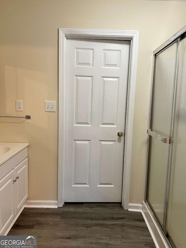 bathroom featuring an enclosed shower, vanity, baseboards, and wood finished floors