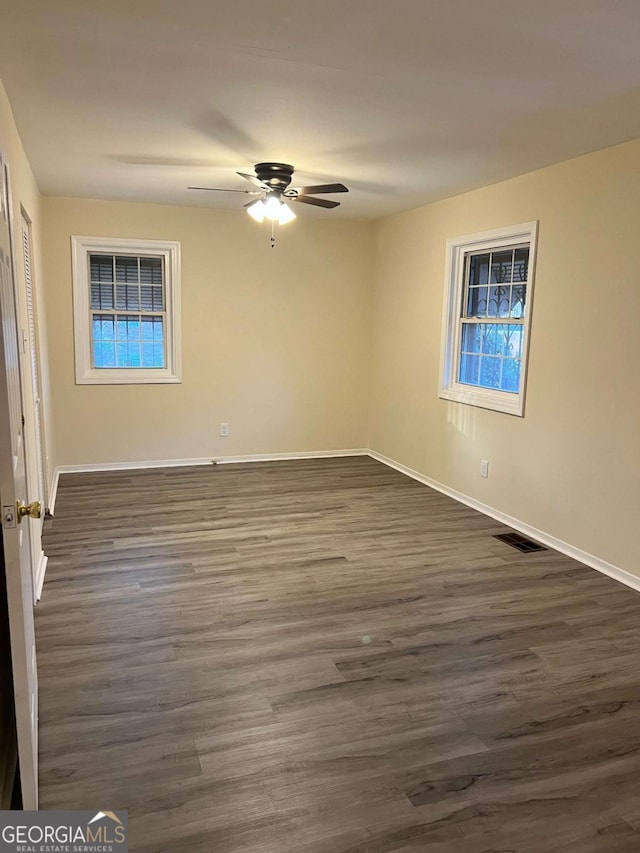 empty room featuring ceiling fan, dark wood-type flooring, visible vents, and baseboards