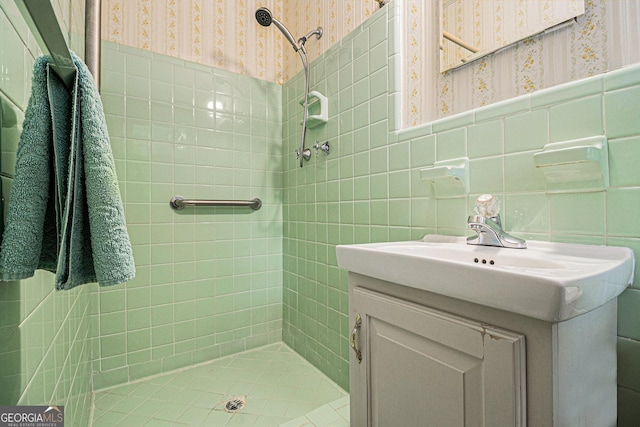 full bathroom with tile walls, vanity, wainscoting, a tile shower, and wallpapered walls