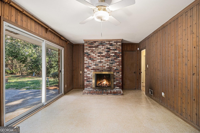 unfurnished living room featuring visible vents, ornamental molding, a brick fireplace, ceiling fan, and wooden walls