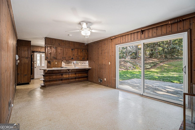 kitchen with ceiling fan, wooden walls, light countertops, and light speckled floor