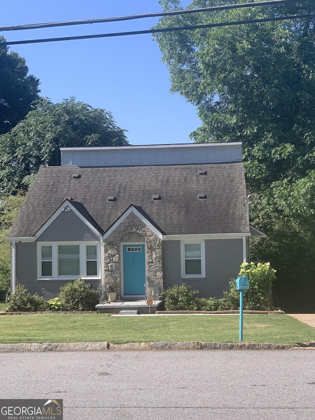 view of front of home featuring stone siding, a front lawn, and roof with shingles