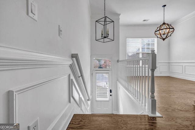 entryway featuring a chandelier, crown molding, plenty of natural light, and a decorative wall