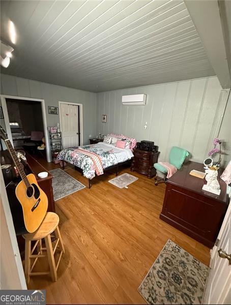 bedroom with a wall unit AC and wood finished floors