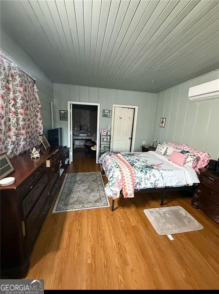 bedroom with wooden ceiling, a wall mounted air conditioner, and wood finished floors