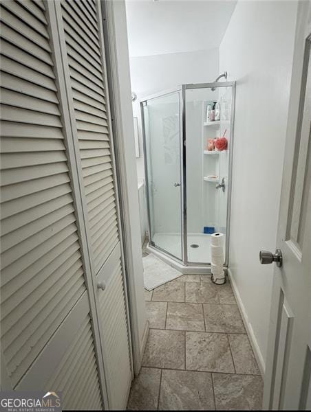 full bathroom with baseboards, a closet, stone tile flooring, and a stall shower