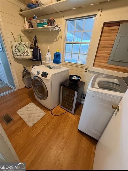 clothes washing area featuring visible vents, light wood-style floors, washer and dryer, laundry area, and electric panel