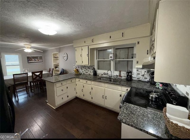 kitchen featuring electric stove, dark wood-style floors, dark stone countertops, a peninsula, and a sink